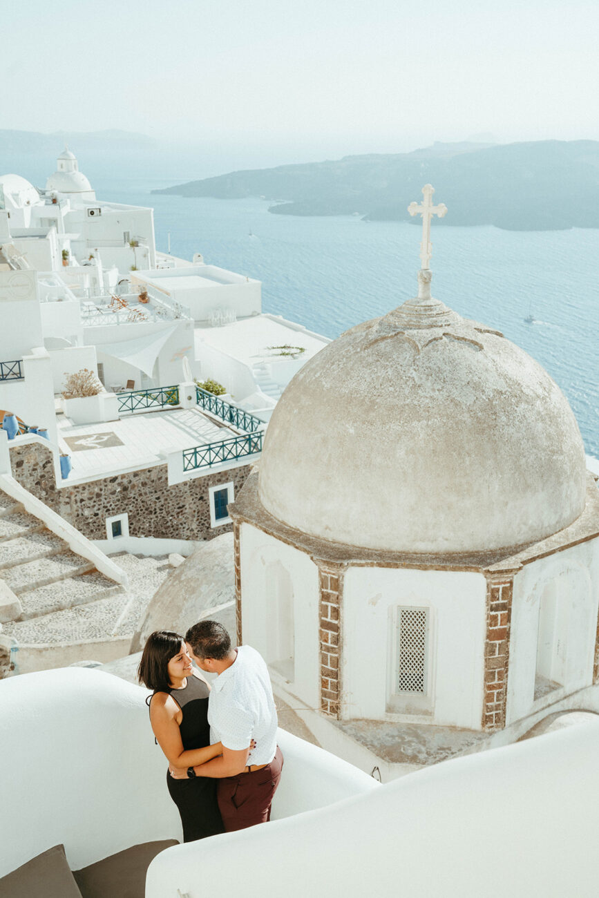 Couple standing on the stairs in front of a chapel overlooking the ocean in in santorini